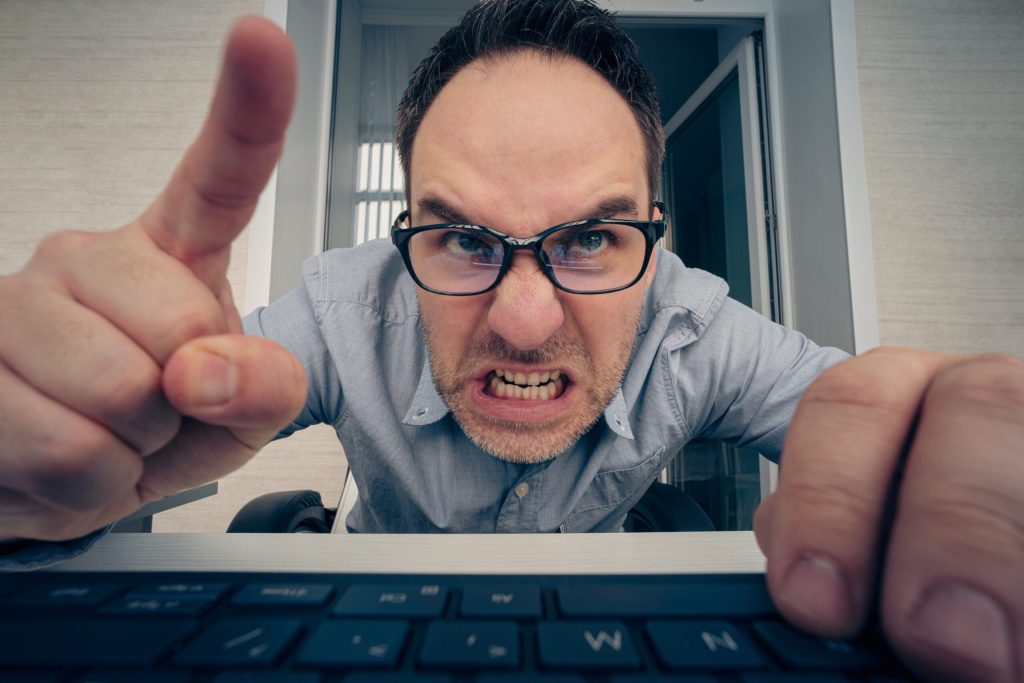 angry hayter writes negative comments on the social network. Negative emotions of businessman employee in front of a computer. malice and hatred concept. offended nerd reads the message on website.